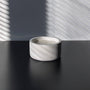 A minimalist, multi-wicked scented candle in a round, smooth concrete vessel. The candle is placed on a dark surface, with soft shadows cast by window blinds against a neutral wall. The clean, simple design emphasizes the modern and tranquil ambiance of the space.