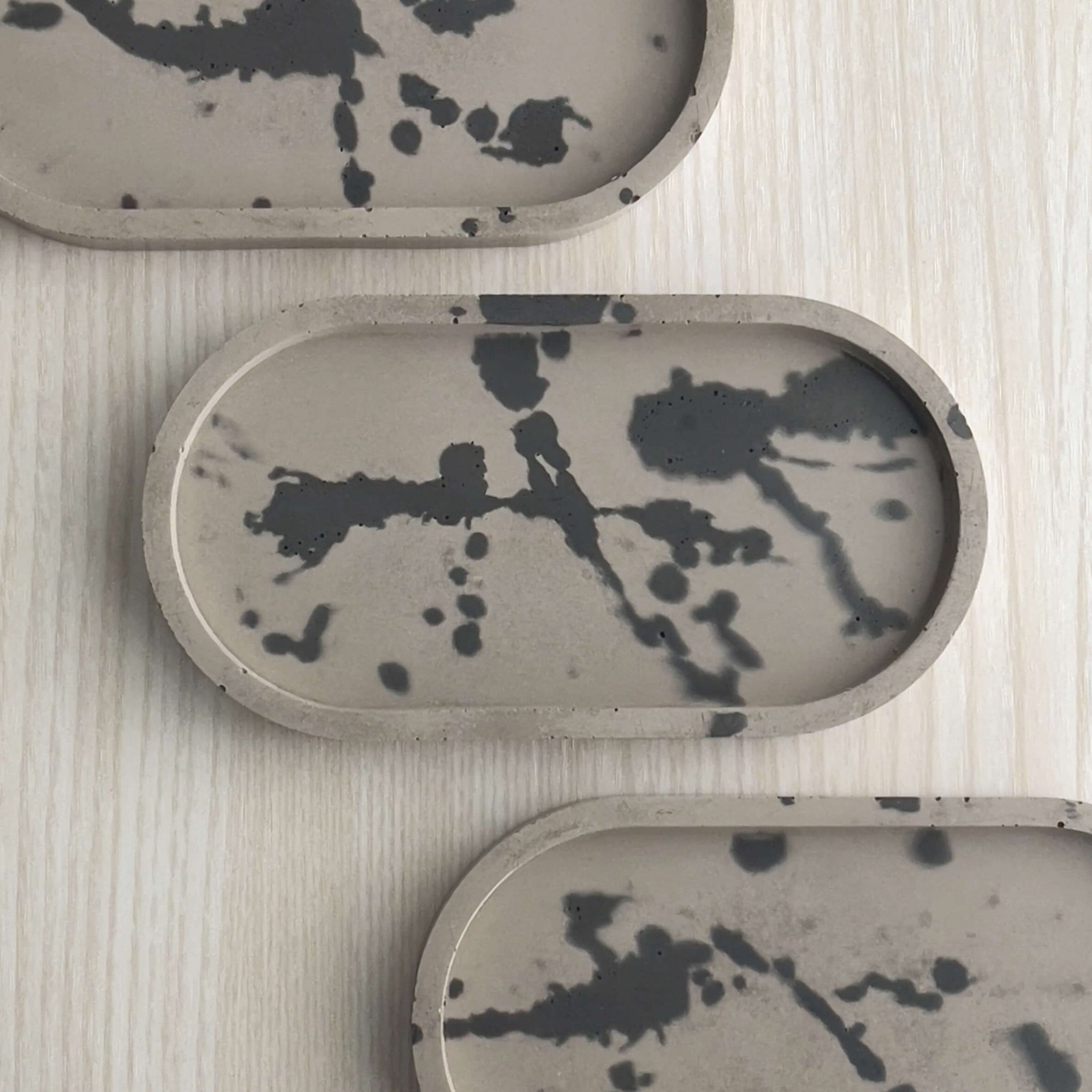 Group of concrete trinket trays in wenge with abstract splatter design in off-black.