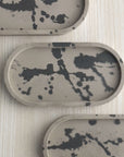 Group of concrete trinket trays in wenge with abstract splatter design in off-black.