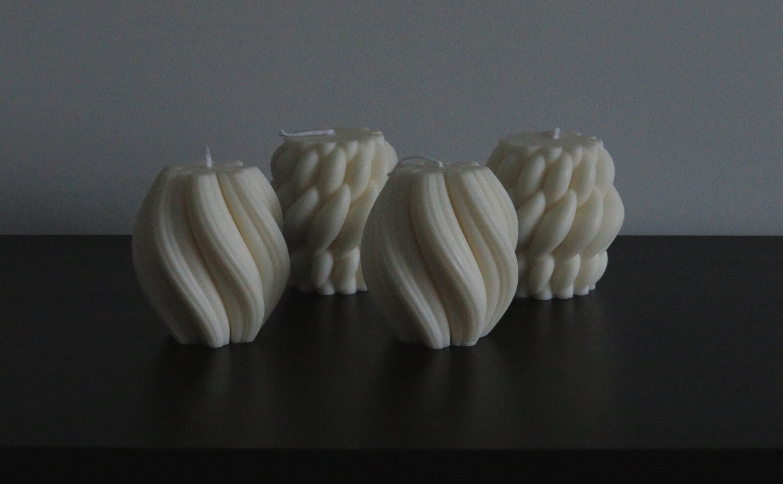 Minimalist sculptural candles with elegant, twisted designs, arranged on a dark surface, showcasing intricate textures and soft ivory tones for modern home decor.