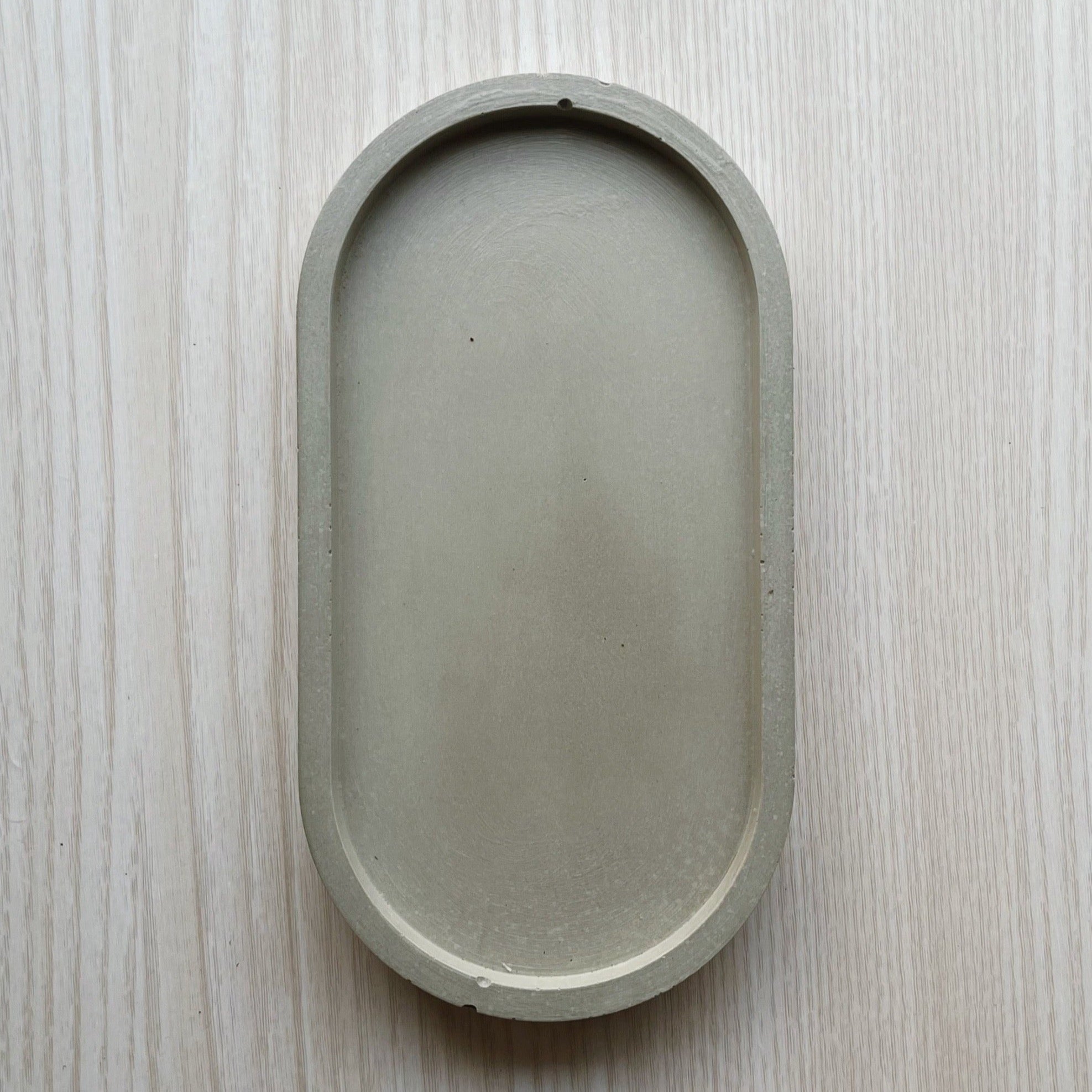 Oval (pill shaped) concrete trinket tray in natural grey.