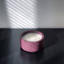 A minimalist, multi-wicked scented candle in a round, deep plum-colored concrete vessel. The candle sits on a dark surface, with soft, diagonal shadows from window blinds cast on the background wall, enhancing the modern, serene aesthetic.