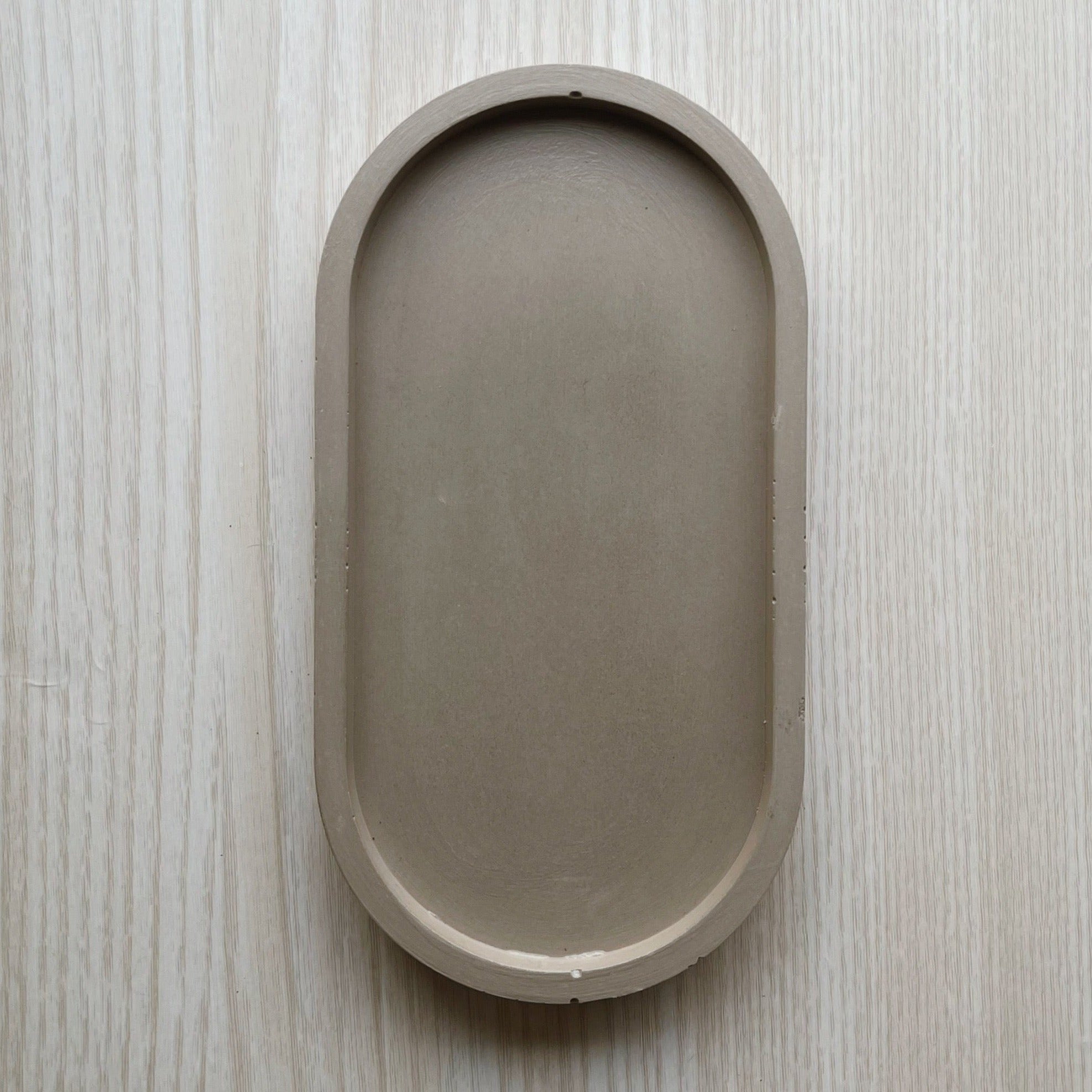 Oval (pill shaped) concrete trinket tray in taupe.